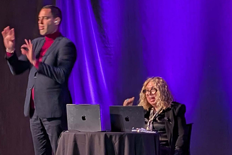 professor kris gutierrez sitting on stage presenting research findings with a sign language interpreter on the left