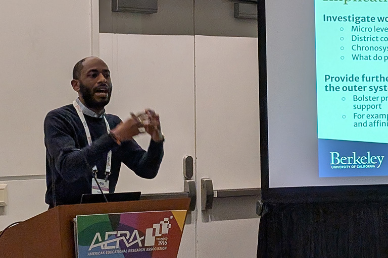 doctoral student aukeem ballard standing at podium gesturing with his hands as he discusses his research