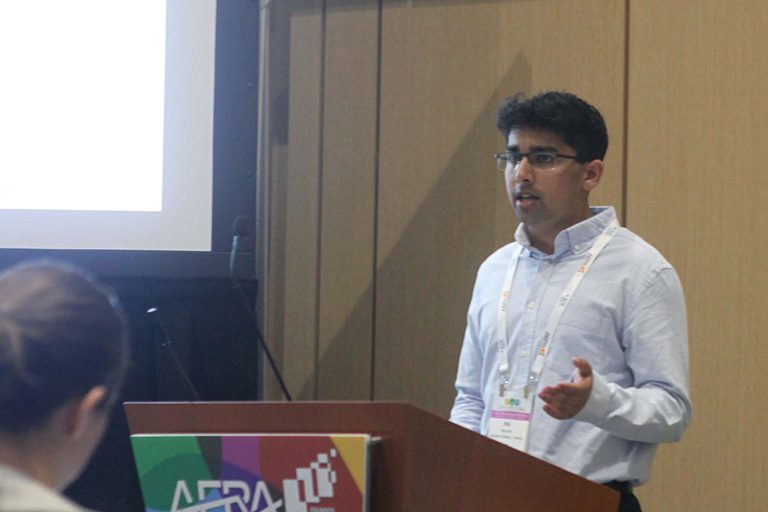 undergraduate student Ritik Sinha standing a podium presenting research findings