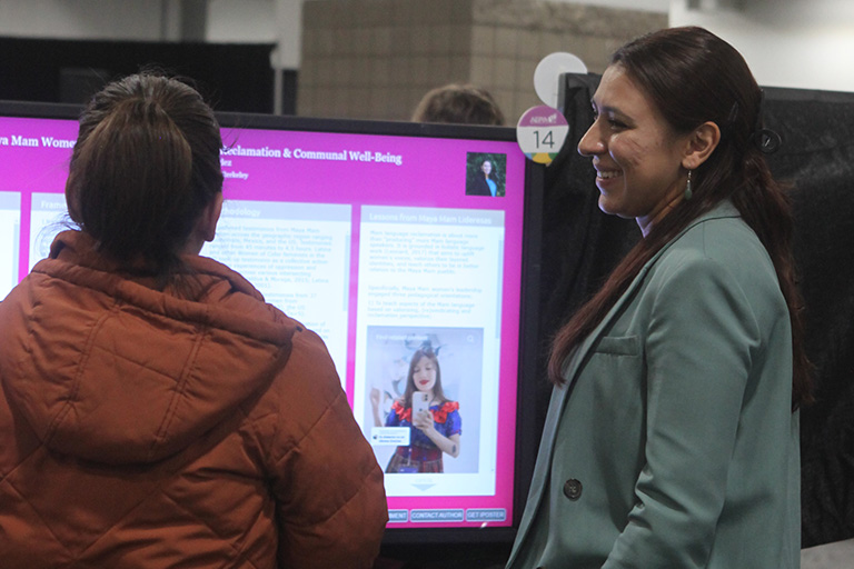 doctoral student cristina mendez standing in front of her poster and talking about her findings with another person