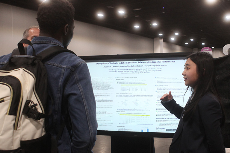 linwei yu standing in front of her poster explaining the research findings to two people