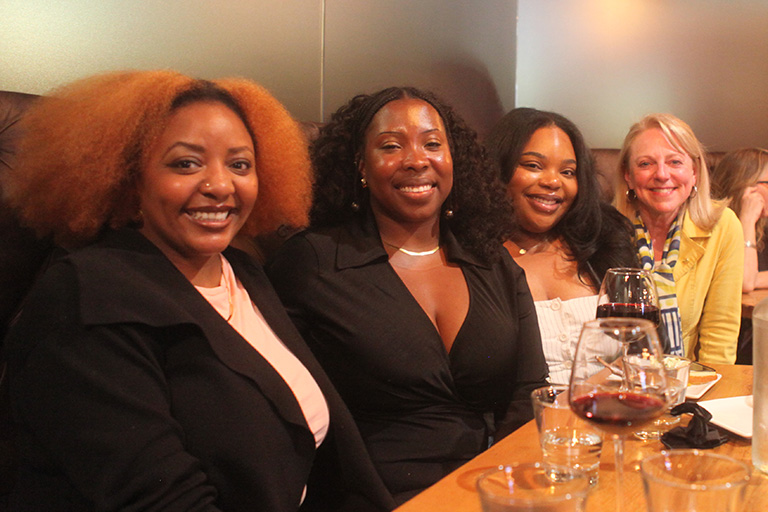 four people sitting next to each other at a table all smiling at camera