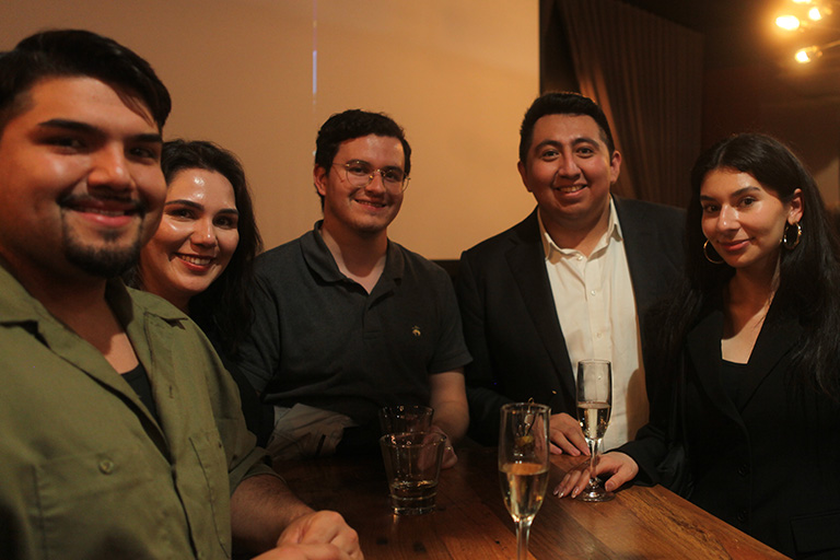 five people standing around a high table smiling at camera
