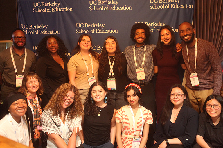 fourteen people in two lines standing in front of the u c berkeley school of education back drop smiling at camera