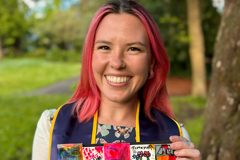 student aimee eagle holding a colorful cloth and smiling at camera