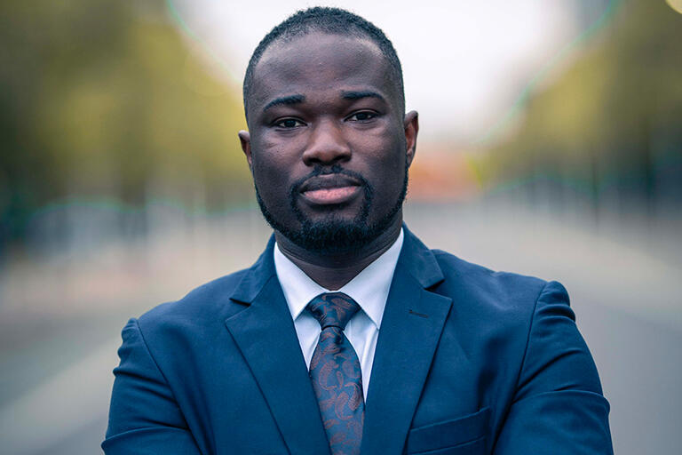 master's degree student eric assan looking at camera with arms crossed