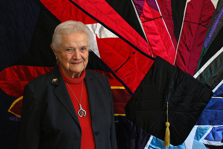 professor emerita k patricia cross standing in front of a quilt made from her regalia