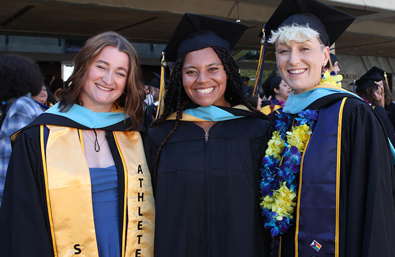 three students who earned their masters degree in education standing next to each other smiling at camera
