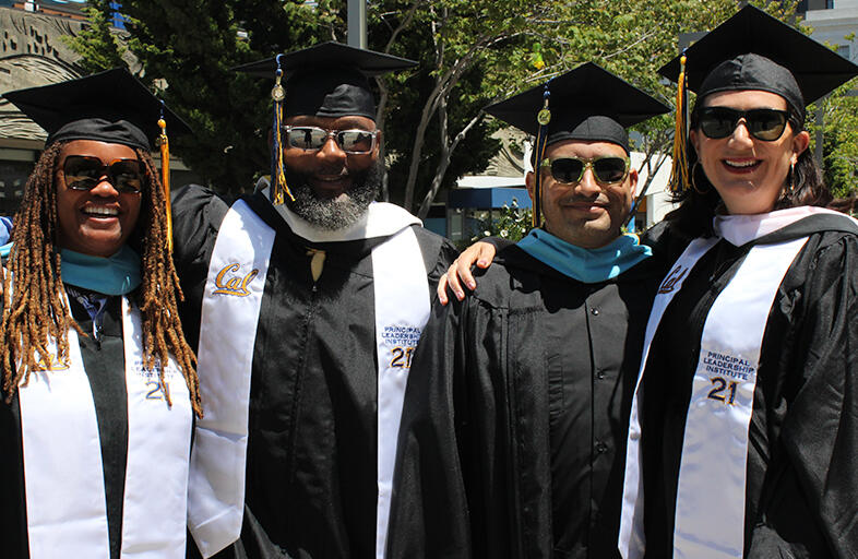 four graduates dressed in their regalia smiling at camera