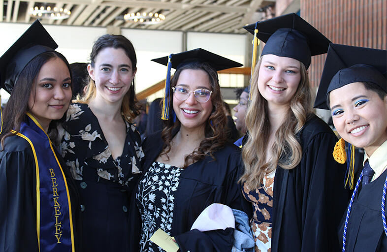 five graduates dressed in their regalia smiling at camera