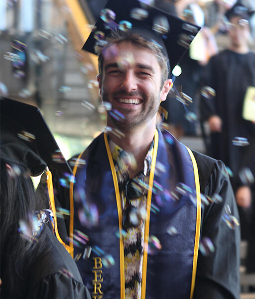 a graduate walking into the ceremony smiling with bubbles floating in front of him