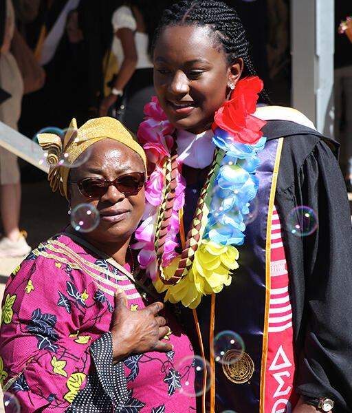 a master's degree student wearing regalia smiling and standing with a family member