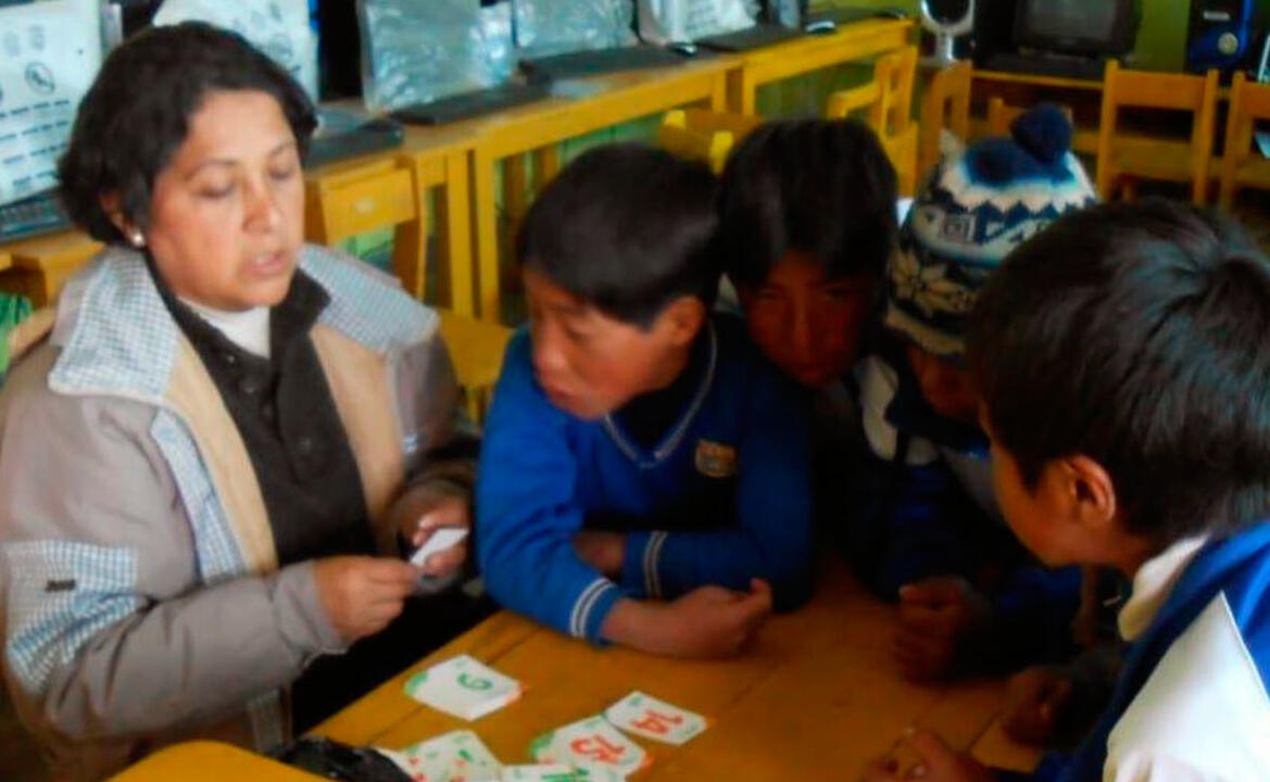 an adult and four schools children gathered around a desk playing a card game