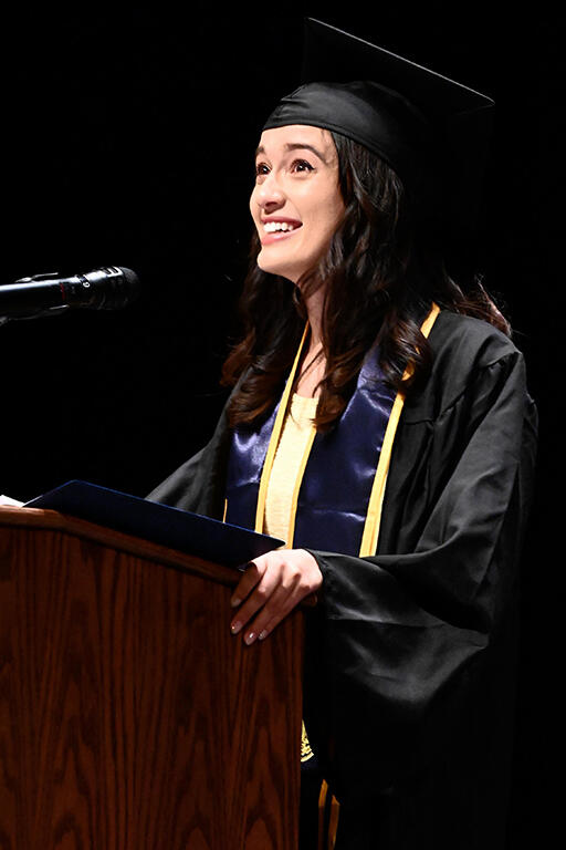 emma rose neal wearing bachelor's degree regalia standing at podium delivering speech