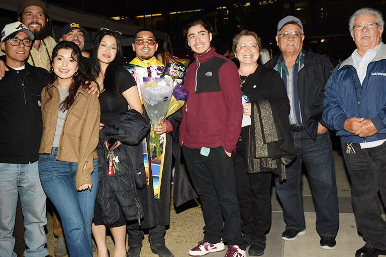 a graduate holding flowers and flanked by nine friends and family everyone smiling at camera