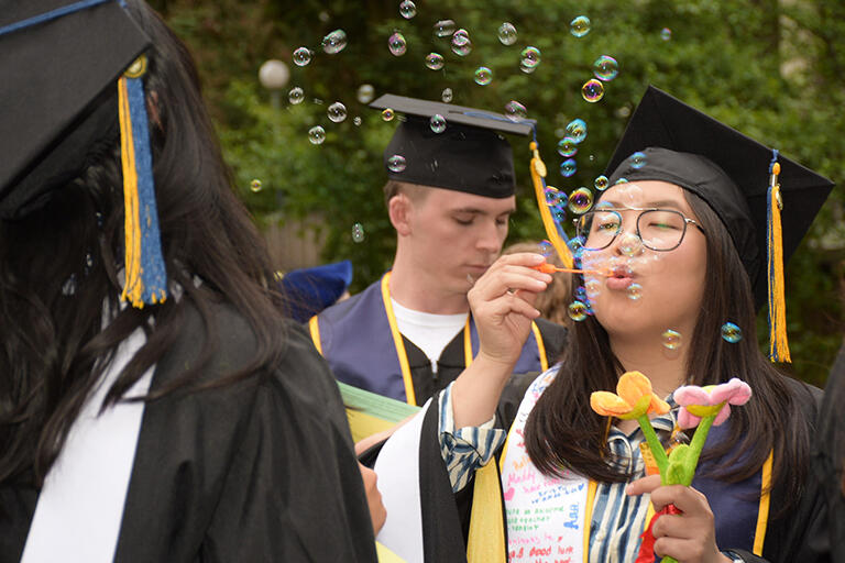student wearing their regalia and blowing small bubbles