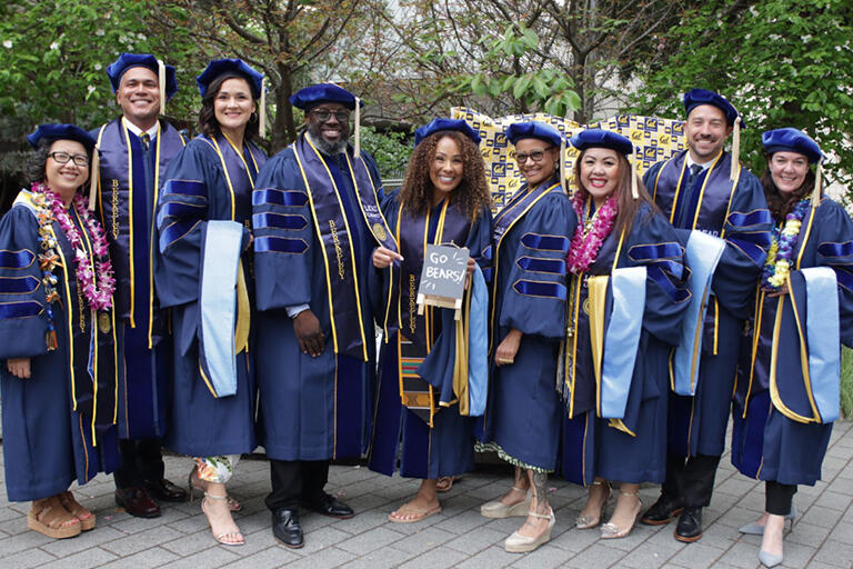 nine graduates of the E D D program wearing their blue regalia standing next to each other all smiling at the camera