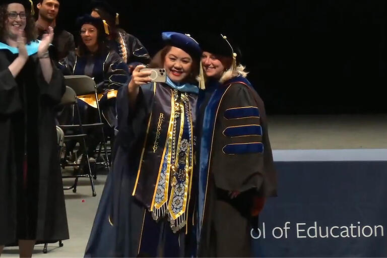 a student pauses on stage to take a selfie with Dean Michelle Young