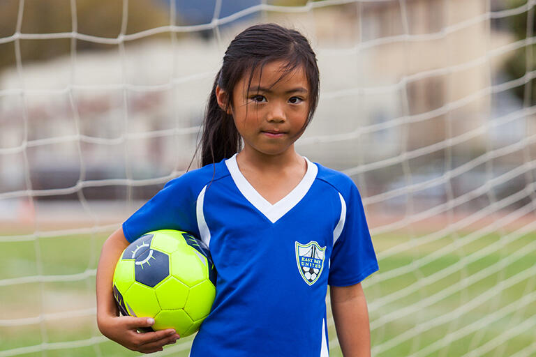 first grade girl holding soccer ball under right arm look seriously into the camera
