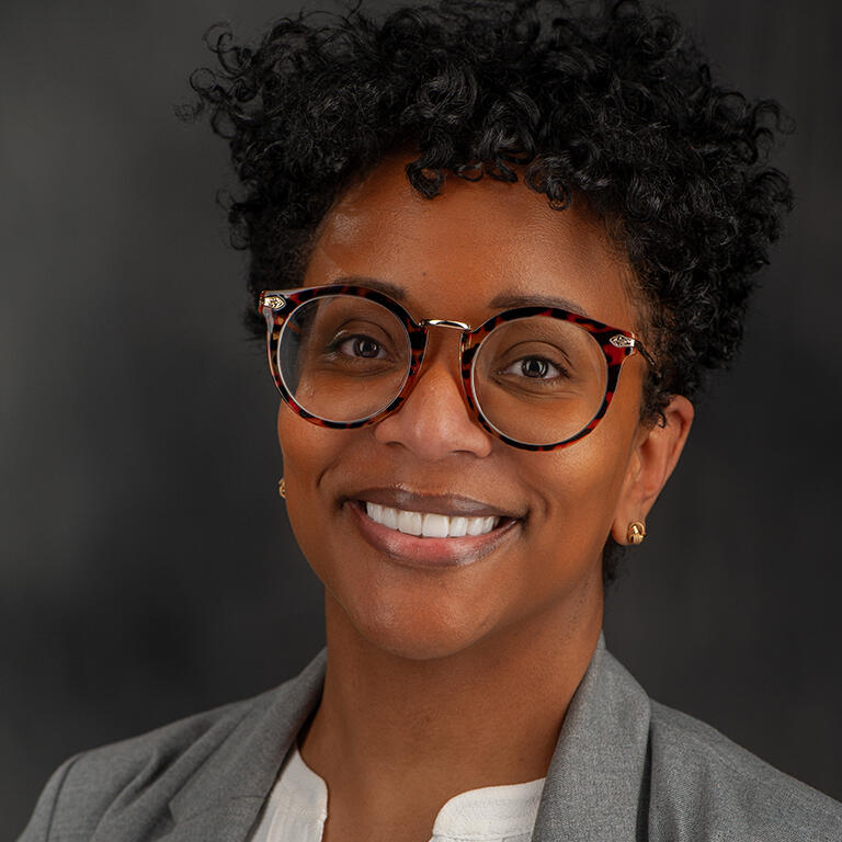 assistant professor dana miller cotto smiling at camera wearing white blouse and gray coat