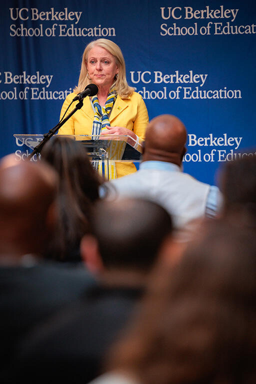 michelle young at the podium speaking to the audience standing in front of a back drop with the u c berkeley school of education logo