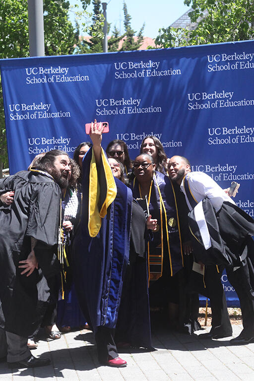 seven graduates and a faculty member bunched together in front of u c berkeley school of education backdrop to take a selfie