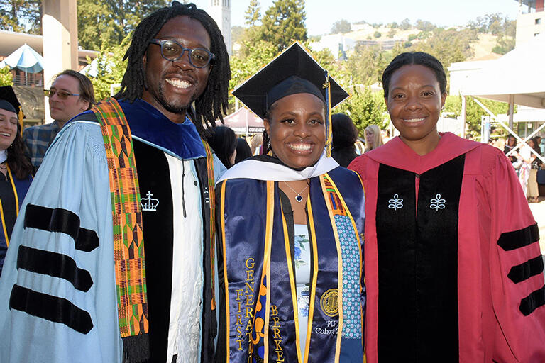 a graduate standing in the middle with professor travis bristol on the left and professor tolani britton on the right and all three are smiling at the camera