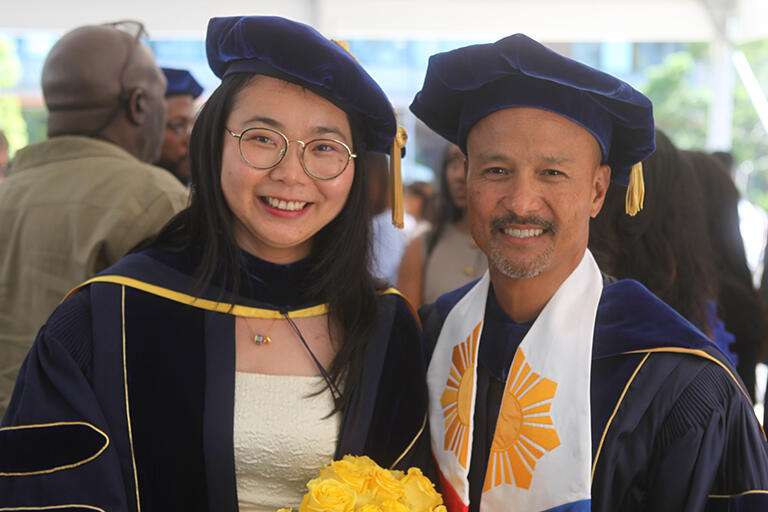 a graduate in their regalia with professor zeus leonardo on the right and both are smiling at the camera