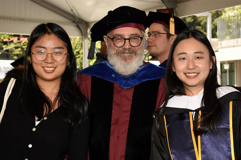 professor mark wilson standing with two people on either side including the person on the right wearing their regalia and everyone is smiling at the camera