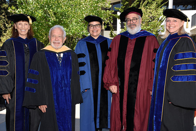 five faculty members wearing their regalia standing next to each other smiling at the camera and they are glynda hull robert reich lisa garcia bedolla mark wilson and michelle young