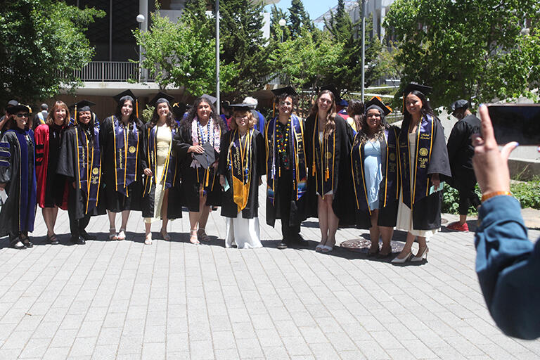 nine bachelor's of science degree students standing next to each other wearing their regalia with two faculty members next to them and everyone is smiling at the camera