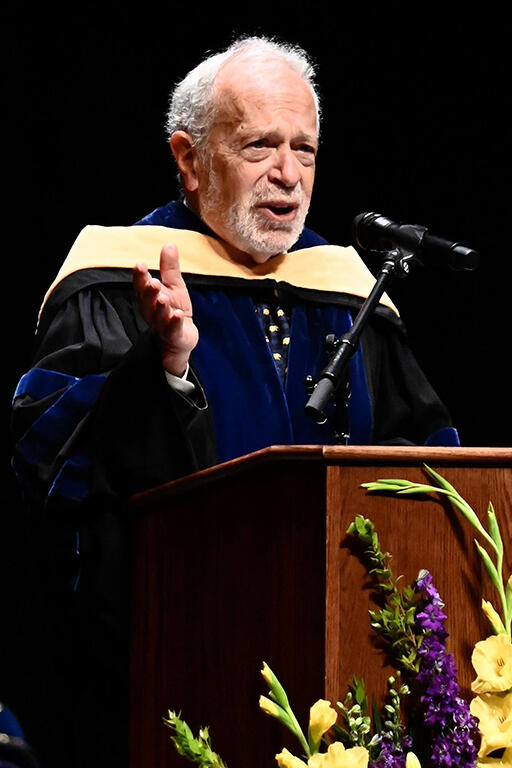 robert reich standing at podium delivering keynote address with right hand slightly raised