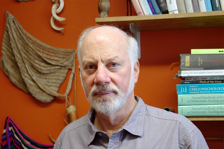 image of professor geoffrey sax with background of books artifacts from papua new guinea