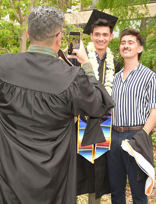 master's degree student standing next to someone both smiling at another person taking their picture with a phone