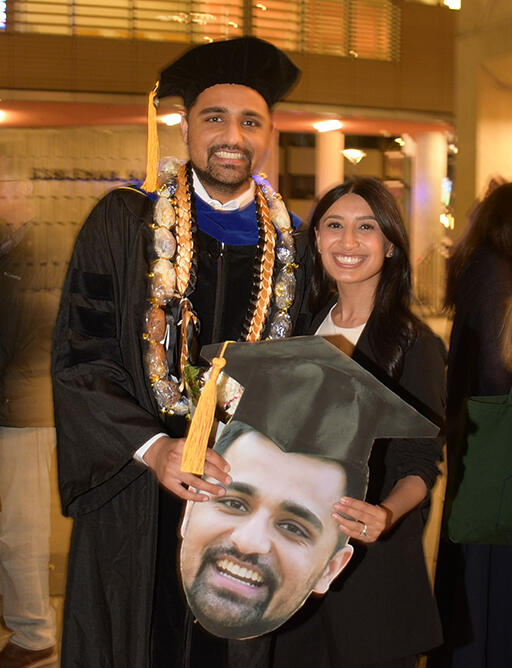 graduate ali bhatti standing with  another person both smiling at camera and holding an oversized photo of ali's face