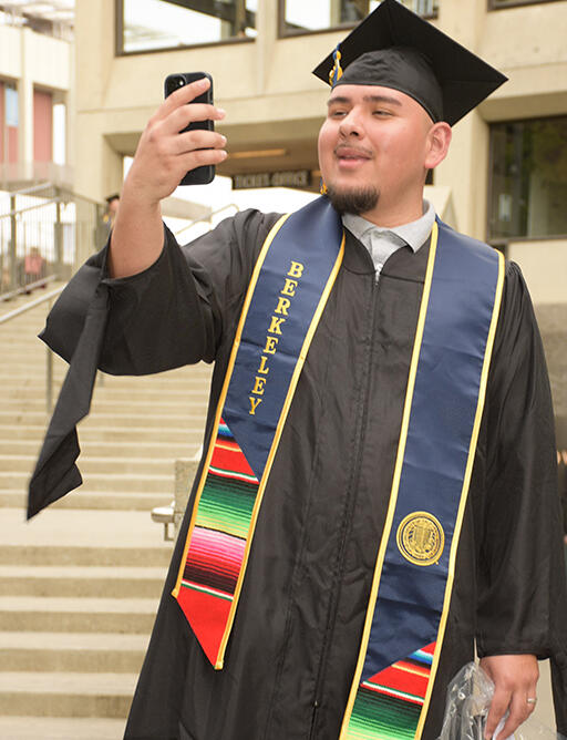master's degree student holding phone up as if taking a selfie or face timing someone